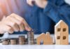 Architect’s Touch Turns Box Into Fortune Hand stacking coins beside wooden house models
