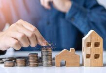 Hand stacking coins beside wooden house models