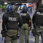 Police officers in riot gear stand on a city sidewalk at night