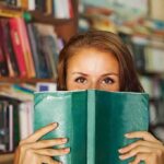 Woman holding a green book in front of her face in a library