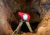 Record Shaken: World’s Deepest Cave Math Caver in red jacket rappelling into a rocky cave entrance