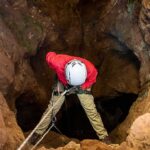 Record Shaken: World’s Deepest Cave Math Caver in red jacket rappelling into a rocky cave entrance