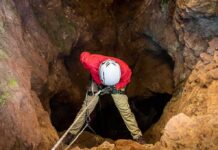 Caver in red jacket rappelling into a rocky cave entrance