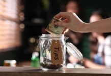 Madison Grab? Tips, OT Still Taxed Hand placing cash into a tip jar on a counter