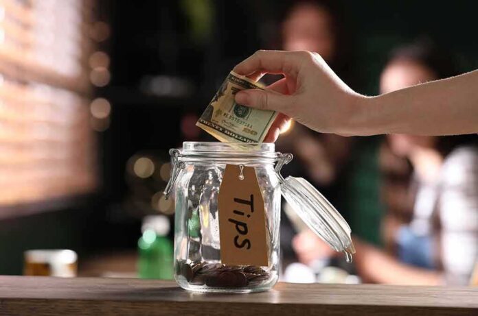 Hand placing cash into a tip jar on a counter