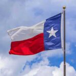Texas state flag waving on a pole against a cloudy sky