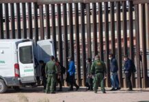 Sixteen Months, Zero Releases – Catch-And-Release Killed Border agents escort a group near a tall fence and a patrol van