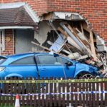Blue car crashed into brick house wall