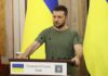 Zelensky Targets Ex-Aide – Punishes Dissent Man at a podium with Ukrainian flags