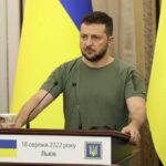 Zelensky Targets Ex-Aide – Punishes Dissent Man at a podium with Ukrainian flags