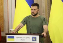 Zelensky Targets Ex-Aide – Punishes Dissent Man at a podium with Ukrainian flags