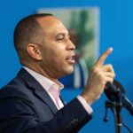 Man speaking at a microphone with raised finger