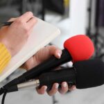 Beijing Squeeze Ends? Trump Bets Big Journalist holding two microphones while writing in a notebook