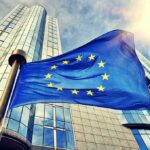 Massive EU Overhaul – Brussels Power Grab Looms European Union flag waving in front of modern glass office buildings