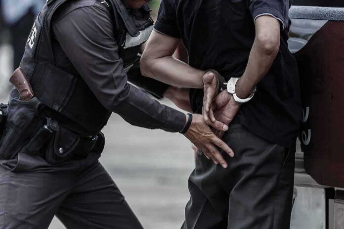 shutterstock_665013085 Police officer handcuffing a person against a vehicle
