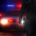Police officer stands before patrol car with flashing lights at night