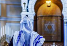 Rabbi Wins — Volunteers Back On Guard Person in white and blue prayer shawl facing ornate interior