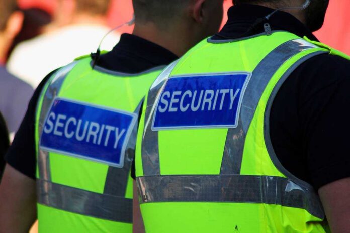 Image,Of,Two,Male,Security,Guards,With,Bright,Tops,On. Two security personnel wearing high visibility vests with SECURITY printed on the back