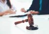 HR Boss Accused – Family Threats, Pay Slashed judge's gavel on table with people discussing documents in background