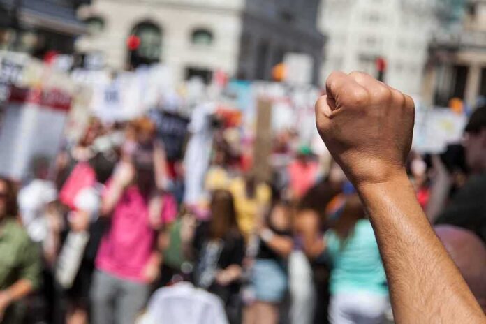 shutterstock_1135501646 Raised fist in foreground at a crowded street protest