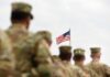 Insider Wagers EXPOSED – Uniforms On Notice U.S. flag flying above a formation of soldiers in uniform