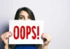 Woman holding a sign that says OOPS in red