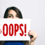 Woman holding a sign that says OOPS in red