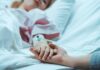 Autonomy Or State-Approved Exit? Patient in hospital bed with IV line holding a visitor's hand