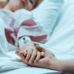 Autonomy Or State-Approved Exit? Patient in hospital bed with IV line holding a visitor's hand