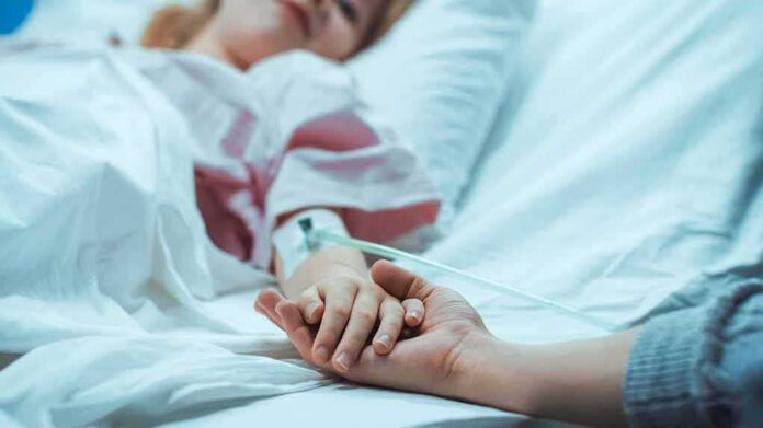 shutterstock_1181842840 Patient in hospital bed with IV line holding a visitor's hand