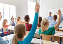 Students raise hands in a classroom with a teacher at the front