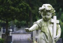 Weathered statue of a child angel holding a cross in a cemetery