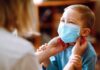 Ontario Builds Vaccine Dossiers On Kids child wearing a surgical mask being adjusted by an adult