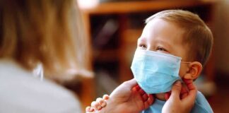 child wearing a surgical mask being adjusted by an adult