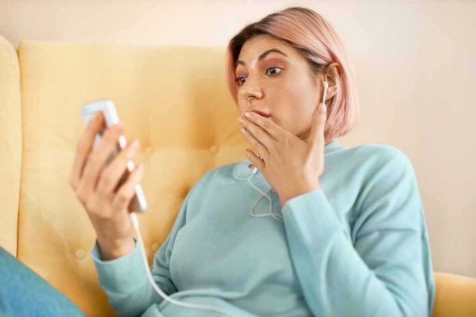 shutterstock_1784166275 Person with earbuds looking at phone in surprise on a yellow couch