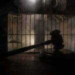 Judge’s gavel in silhouette before prison bars