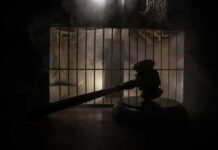 Judge’s gavel in silhouette before prison bars
