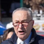 older man speaking outdoors wearing red glasses