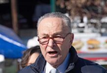 older man speaking outdoors wearing red glasses