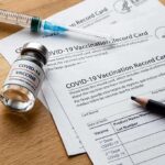 Did Pfizer Oversell Safety? Blockbuster Deception Showdown COVID-19 vaccine vial with syringe and vaccination record cards