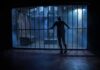Silhouette of a person gripping prison cell bars