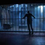 Silhouette of a person gripping prison cell bars