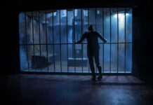 Silhouette of a person gripping prison cell bars