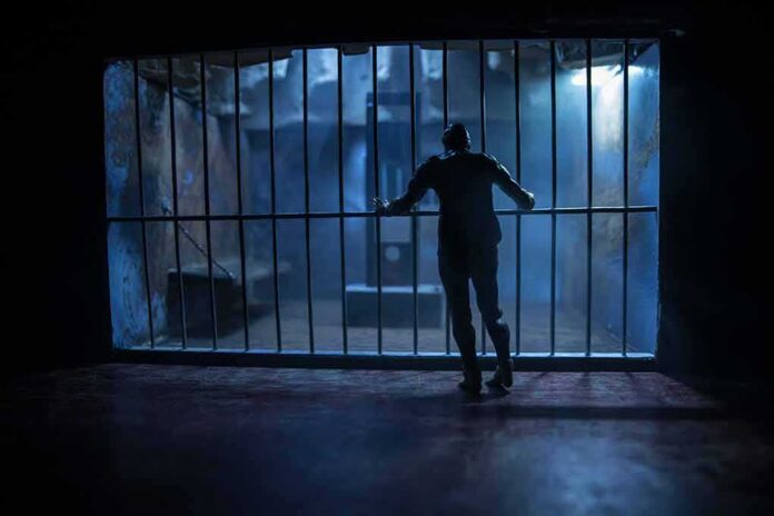 Silhouette of a person gripping prison cell bars