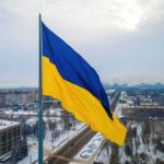 Massive Barrage – Blackouts Sweep Kyiv After Strikes Ukrainian flag over snowy cityscape