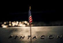 Silent Bump: Troop Deaths Recounted Small American flag on a memorial with bokeh lights at night