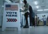 Vote here sign at a polling station with people in line