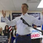 Rand Paul speaking at a campaign event with supporters holding signs