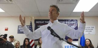 Rand Paul speaking at a campaign event with supporters holding signs